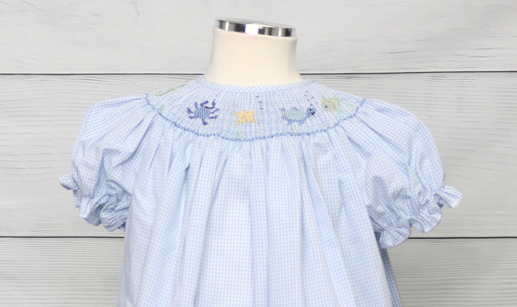 
Elevate your little one's wardrobe with this enchanting blue gingham smocked dress. Expertly crafted with handmade smocking, this charming bishop dress features intricate geometric patterns and delicate tiny sea creatures, adding a whimsical touch to its classic design. The combination of timeless blue gingham and the playful, hand-embroidered details makes this dress perfect for any special occasion. Ideal for capturing attention and creating memorable moments, this dress blends elegance and fun in a way 